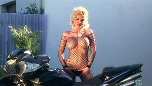 Big-chested platinum-blonde teases on a motorcycle in fishnet
